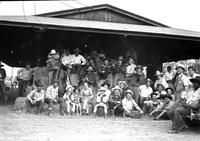 [Group of people, including a musical band, children & Rodeo people sitting or standing on bales]