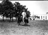 [J. Wills on dark horse wearing silver saddle. Trees and stadium in background]