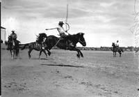 [Unidentified Cowboy riding and staying with his bronc as three mounted cowboys hover nearby]