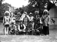 [California Frank among a group of eight Indian men (Sioux) and tipis, trees in background]