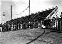 [View of grandstand crowd and other onlookers watching the action in the arena]