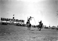 [Unidentified Cowboy standing on stationary horse throwing rope loop over passing horseback rider]