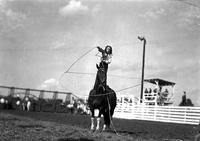 [Unidentified little cowgirl standing on stationary horse spinning a large rope loop around herself]