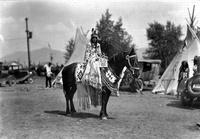 [Indian women atop horse with tipis and cars in background]