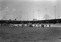 [Indian men and women dancing in arena; spectators in bleachers behind them]