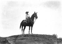 [Unidentified older cowgirl posed atop horse]