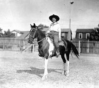 [Unidentified Cowgirl on horse with house in background]