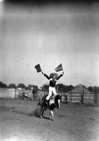 [Little Tin Horn Hank Keenen doing hippodrome stand holding American Flags above head]