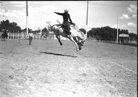 [Cecil Henley riding and staying with his airborne bronc "Cry Baby" in center of arena]