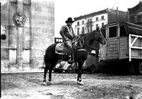 [Unidentified Cowboy on horseback holding rope loop in hand in front of rodeo entrance]