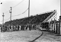 [View of grandstand crowd and other onlookers watching the action in the arena]