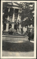 [2 women standing near a statue of an Indian killing a buffalo (all are in front of a building)