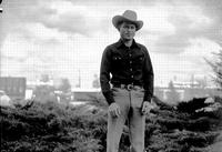 [Unidentified cowboy standing in front of bushes]