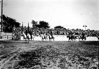 [Riders in pairs passing in front of grandstand; lead riders bearing flags]