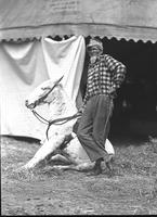 [Unidentified Rodeo clown posed with mule in front of tent]