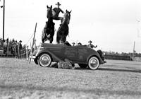 [Unidentified Cowboy doing Roman Stand jump over auto with Clown beneath car]