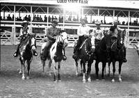 [Cremer at the center of two cowboys, one cowgirl, and a man in a suit; all on horses]