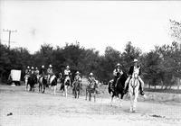 [Line of unidentified cowboys, cowgirls & children on ponies trail riding]