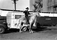 [Unidentified cowboy posed on horse with George Pitman trailer in behind]