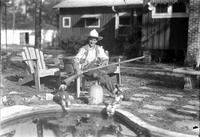 [Unidentified man seated in wooden chair holding a long rifle and crossed pistols in his lap]