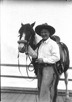 [Unidentified cowboy smoking and standing beside horse]