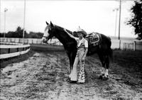 [Young unidentified Cowgirl standing with horse wearing trick saddle]
