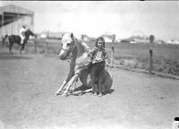 [Little girl, Jean Graham, standing by her sitting pony]