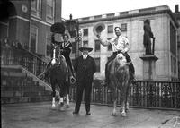 [Possibly Alice Sisty and unidentified Cowboy on horses waving hats with man standing between them]