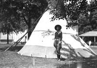 [Single unidentified cowgirl standing in front of tipi]