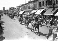 [Indian men on horseback parading down crowded street]