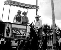 [Possibly Everett Colborn on horse standing in front of raised stand holding Gene Autry and another]