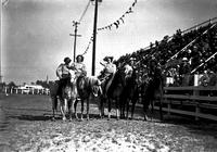 [Group of five unidentified cowgirls on horseback in line near press box of grandstand]