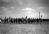 [Large group of Indian men & one child and one cowboy (possibly Ricker) on horseback all in arena]