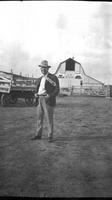 [Possibly Clarence Parker in fedora, suit and tie with barn marked with "C.P. Ranch" in background'