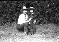 [Johnnie Lee Wills kneeling next to unidentified little girl in western outfit in front of bushes]