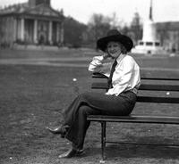 [Possibly Iva Del Jacobs sitting on park bench with building behind]