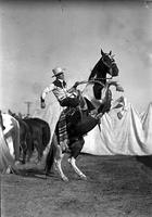 [Possibly Cecil Cornish on rearing Pinto "Smokey" wearing silver mounted tack serape behind saddle]