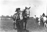 [Possibly Zach T. Miller in colorful vest and scarf standing beside horse]