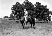 [Johnnie Lee Wills with hat in hand on dark horse wearing silver mounted saddle]