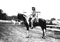 [Unidentified cowgirl posed on horse on racetrack]