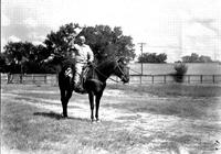 [Unidentified Cowboy with hat in hand over head on horse; trees and fence in background]