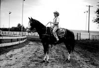 [Young unidentified Cowgirl mounted on horse wearing trick saddle]