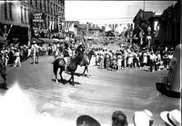 [Two mounted cowboys making turn from main street]