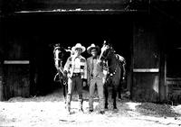 [Gene Autry and Col. Jim Eskew and two horses in large barn doorway]