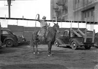 [Possibly Barton Carter atop horse between cars and truck holding rope loop aloft]