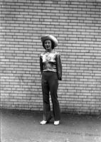 [Unidentified Curly-haired Cowgirl in silk blouse standing in front of brick wall]