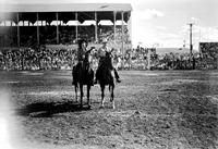 [Unidentified Cowboy and Cowgirl mounted on horseback in front of grandstand]