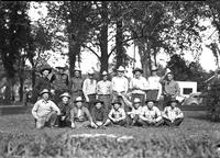 [Group of cowboys sitting and standing in front of trees]