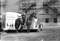 [Unidentified cowboy posed on horse in front of George Pitman trailer and automobile]