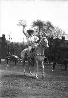 [Possibly Cy Compton raising coiled rope above head with right hand while sitting on horse]